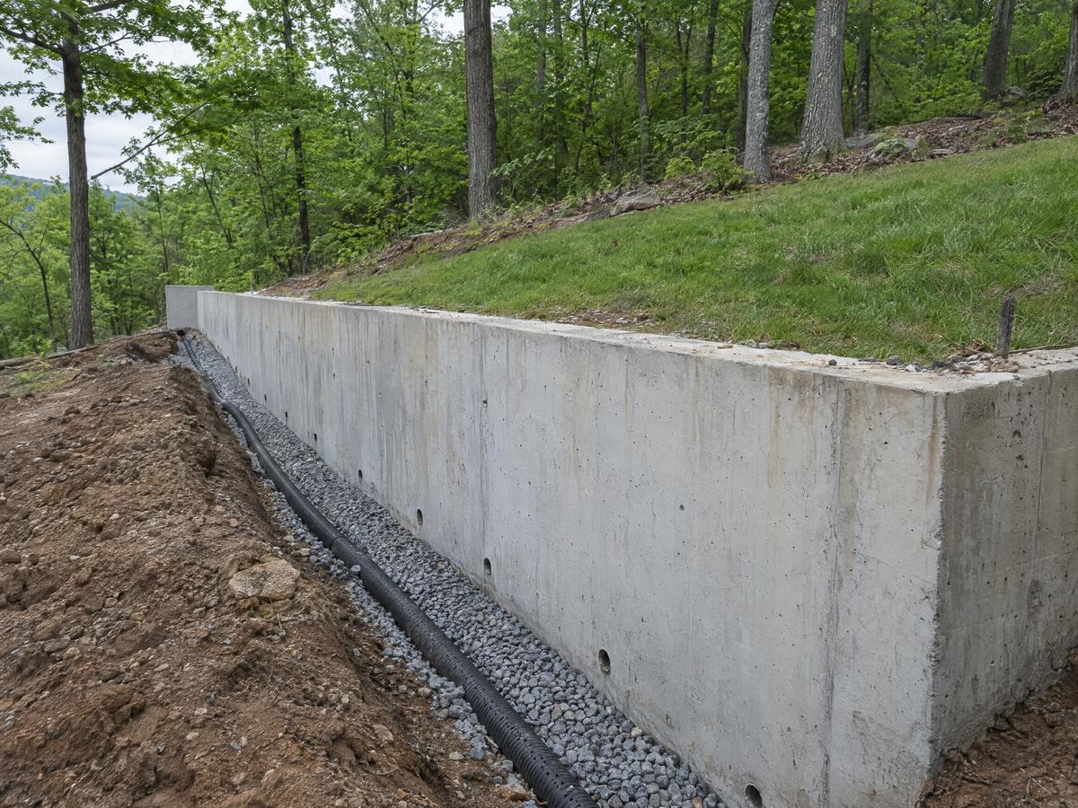 Cast-in-place concrete retaining wall holding a sloped lawn, weep holes along its base and a gravel drain trench behind it