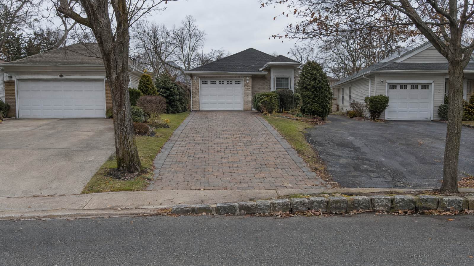 Concrete, paver and asphalt driveways side by side on a suburban street with a granite Belgian block curb